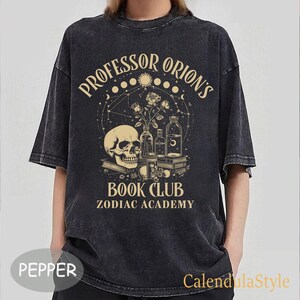 Puede incluir: Camiseta negra de estilo vintage con un dise&ntilde;o gr&aacute;fico que presenta una calavera, rosas y botellas. El texto dice "Professor Orion's Book Club Zodiac Academy".