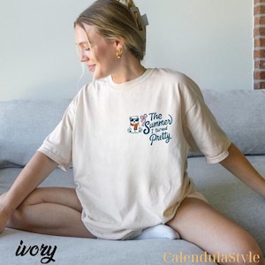 May include: Ivory-colored t-shirt with a small graphic of a bear wearing sunglasses and a scarf, with the text "The Summer I turned Pretty" in blue script. The shirt is a relaxed fit.