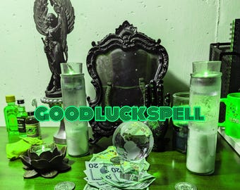 Puede incluir: Un altar verde y negro con velas, un globo terráqueo, dinero y una estatua de un ángel. El texto "GOODLUCKSPELL" está escrito en letras verdes en el altar.