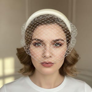 Op de afbeelding: Ivoor kleurige bruidssluier met een gewatteerde hoofdband en een fijne mesh sluier. De sluier valt over het gezicht en cre&euml;ert een zachte, romantische uitstraling. Perfect voor bruiloften en speciale gelegenheden.