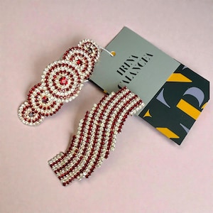 May include: Two decorative hair clips with red and clear crystals. One features concentric circles, the other a wavy pattern. A grey tag with the text "IRINA CALANCEA" is visible in the background.