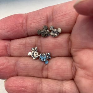 Puede incluir: Un conjunto de cinco dijes de metal plateado con Mickey Mouse y Minnie Mouse. Los dijes son peque&ntilde;os y detallados, perfectos para agregar un toque de magia de Disney a las joyas o manualidades.
