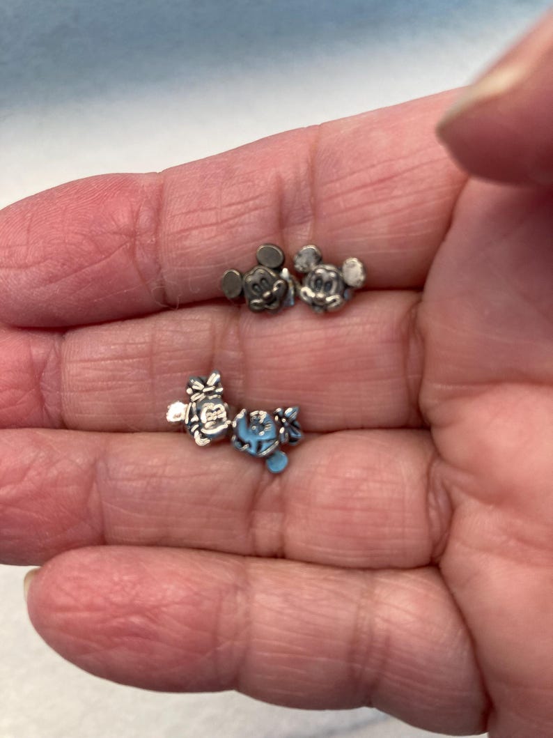 Puede incluir: Un conjunto de cinco dijes de metal plateado con Mickey Mouse y Minnie Mouse. Los dijes son peque&ntilde;os y detallados, perfectos para agregar un toque de magia de Disney a las joyas o manualidades.