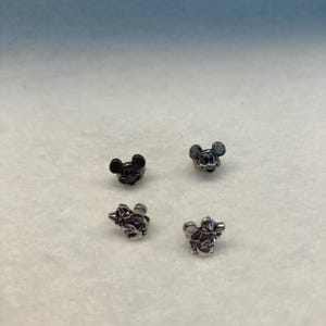 Puede incluir: Cuatro peque&ntilde;os abalorios de metal con los personajes de Mickey Mouse y Minnie Mouse. Dos son plateados y dos son negros.