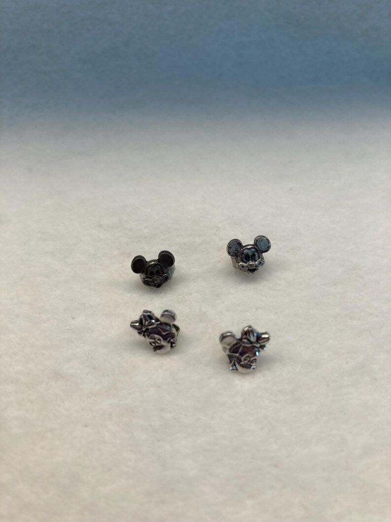 Puede incluir: Cuatro peque&ntilde;os abalorios de metal con los personajes de Mickey Mouse y Minnie Mouse. Dos son plateados y dos son negros.
