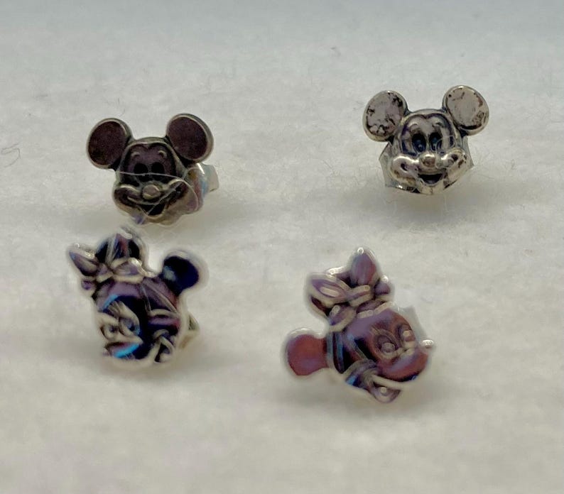 Puede incluir: Cuatro pendientes de bot&oacute;n plateados con los personajes de Mickey Mouse y Minnie Mouse. Los pendientes son peque&ntilde;os y delicados, perfectos para a&ntilde;adir un toque de magia Disney a cualquier atuendo.