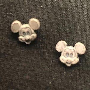 Puede incluir: Dos peque&ntilde;as figuras de pl&aacute;stico de Mickey Mouse de color blanco. Las figuras est&aacute;n mirando hacia adelante con las orejas apuntando hacia los lados. Las figuras est&aacute;n sobre una superficie gris oscuro.