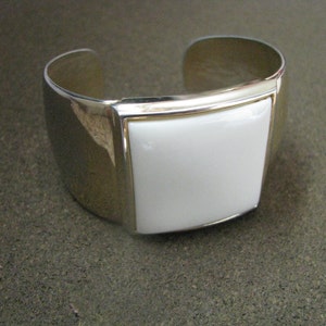 May include: A silver cuff bracelet with a white square-shaped ceramic inlay.