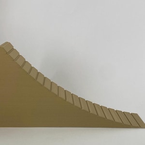 Könnte beinhalten: Ein keilförmiges Objekt in Beige mit einer Reihe horizontaler Rippen entlang seiner geneigten Oberfläche. Das Objekt hat eine abgerundete Oberseite und eine flache Basis. Die Rippen sind gleichmäßig angeordnet und erzeugen ein treppenartiges Aussehen. Das Objekt besteht aus einem festen Material.