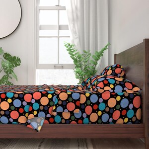 May include: A bed with a black background and colourful polka dots. The bed has a wooden frame and a white headboard. The bedding is made of soft, comfortable fabric.