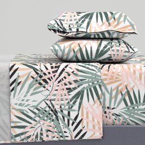 May include: A white bedding set with a tropical leaf pattern in shades of green, pink, and black. The set includes a flat sheet, fitted sheet, and two pillowcases.