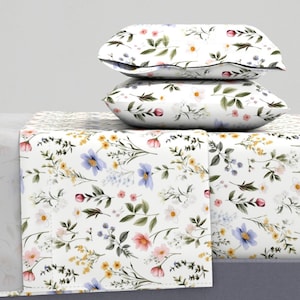Pode incluir: Roupa de cama branca com um padrão floral com flores rosa, azuis e amarelas e folhas verdes.