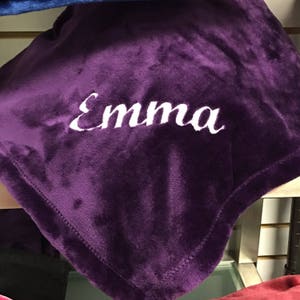 May include: A purple plush blanket with the name "Emma" embroidered in white.