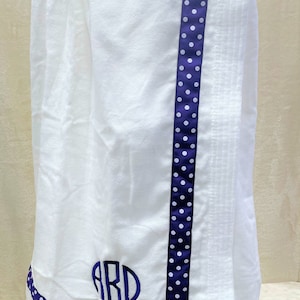 May include: White bath wrap with a purple and white polka dot trim. The wrap has a monogram of the letters "ABD" in a circle.
