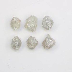 May include: Six rough, unpolished, gray diamonds. The diamonds are various sizes and shapes.