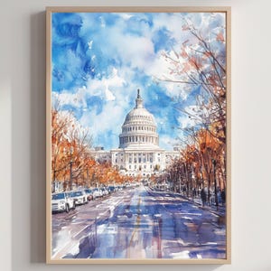 以下が含まれることがあります： ワシントンD.C.にあるアメリカ合衆国議会議事堂の水彩画。秋色の木々に囲まれた建物へと続く道を描いています。空は鮮やかな青色で白い雲があり、絵は額装されています。