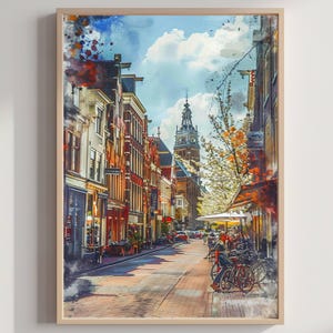 Op de afbeelding: Aquarelprint van een Europese straatscène met gebouwen, fietsen en een kerktoren. Het kunstwerk heeft een warm kleurenpalet met tinten rood, oranje en bruin, en een blauwe lucht met wolken.