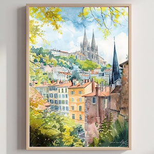 May include: Watercolour painting of a European cityscape featuring a cathedral and buildings with orange rooftops. The artwork is framed in a light wood frame. The sky is blue with white clouds, and green foliage is in the foreground.