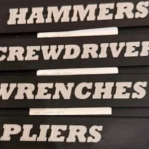 May include: Four rectangular black labels with raised silver lettering. The labels feature the words HAMMERS, SCREWDRIVERS, WRENCHES, and PLIERS in a bold, sans-serif font. Each label is designed for tool organization and identification.
