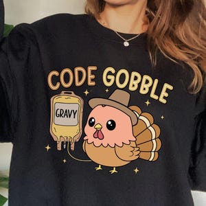 May include: Black sweatshirt with the text "CODE GOBBLE" and a cartoon turkey wearing a hat. The turkey is next to a bag labeled "GRAVY". The design is in shades of brown, orange, and yellow.