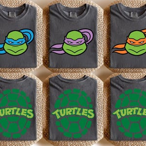 May include: Six dark gray t-shirts with different Teenage Mutant Ninja Turtle designs. Three shirts feature the turtles' faces with blue, purple, and orange masks. The other three shirts have a green turtle shell design with the word "Turtles".