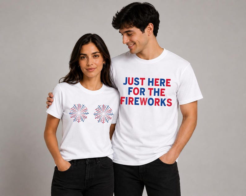 May include: Two white short-sleeved t-shirts. One shirt features two red, white, and blue firework graphics on the chest. The other shirt features the text "JUST HERE FOR THE FIREWORKS" in red and blue block lettering on the chest.