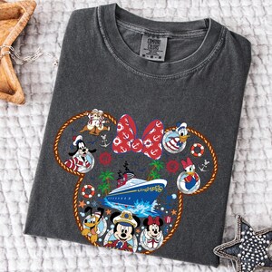 May include: Dark grey t-shirt with a nautical design featuring Disney characters such as Mickey and Minnie Mouse. The design includes a cruise ship, anchors, and a red bow. The shirt is made of a soft material.