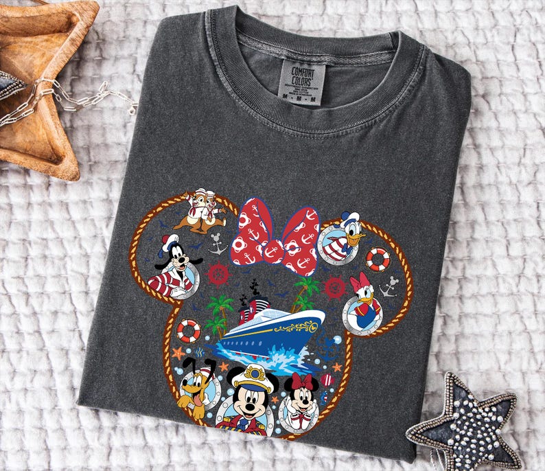 May include: Dark grey t-shirt with a nautical design featuring Disney characters such as Mickey and Minnie Mouse. The design includes a cruise ship, anchors, and a red bow. The shirt is made of a soft material.