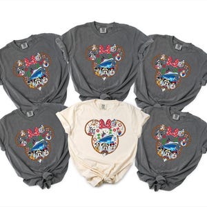 May include: Six t-shirts in shades of grey and cream, each featuring a Minnie Mouse design. The design includes a red bow, a cruise ship, and Disney characters. The shirts are made of soft fabric and have a relaxed fit.