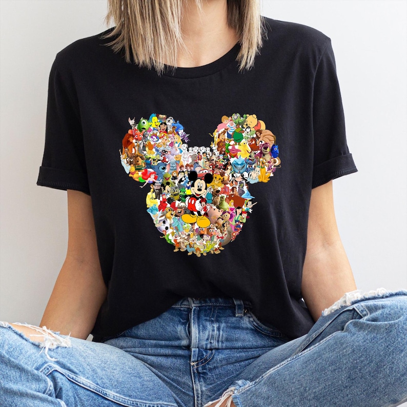 May include: Black t-shirt featuring a colorful collage of Disney characters arranged in the shape of Mickey Mouse's head. The design includes characters like Mickey, Minnie, Donald Duck, and many more. The shirt is made of a soft material.
