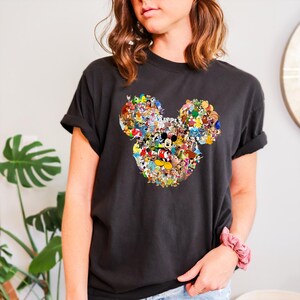 May include: Black t-shirt featuring a colorful Mickey Mouse head design composed of various Disney characters. The graphic is centrally placed on the shirt. The shirt has short sleeves and a relaxed fit, suitable for casual wear.