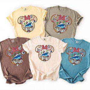 May include: Five short-sleeved t-shirts in yellow, grey, brown, cream, and blue. Each shirt has a Minnie Mouse head design with a red bow and a cruise ship graphic. The design includes cartoon characters.