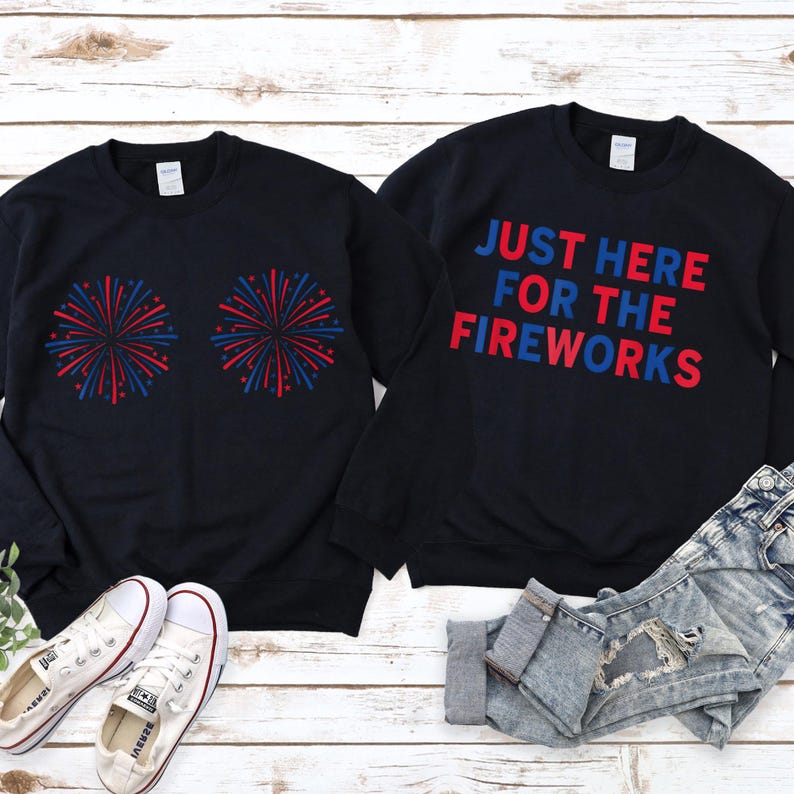 May include: Two black crewneck sweatshirts. One features two red and blue firework graphics. The other displays the text "JUST HERE FOR THE FIREWORKS" in red and blue lettering. A pair of white canvas sneakers and distressed blue jeans are included.