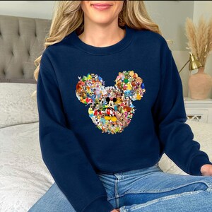May include: Navy blue sweatshirt featuring a Mickey Mouse head design composed of various Disney characters. The graphic includes characters like Mickey, Minnie, Donald, and Goofy, in a colorful collage. The sweatshirt is a crew neck style.