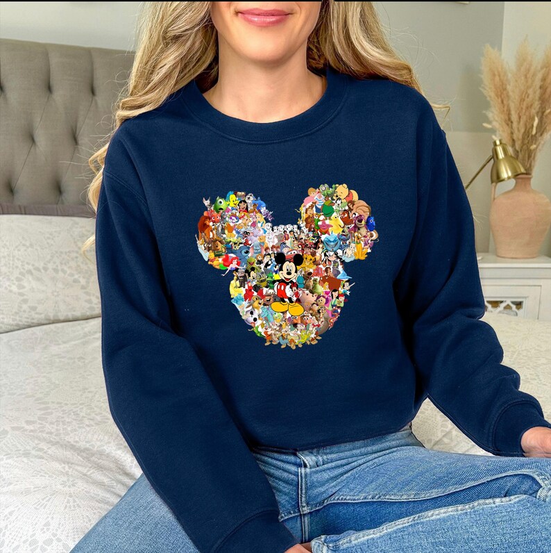 May include: Navy blue sweatshirt featuring a Mickey Mouse head design composed of various Disney characters. The graphic includes characters like Mickey, Minnie, Donald, and Goofy, in a colorful collage. The sweatshirt is a crew neck style.