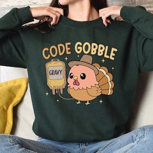 May include: Dark green sweatshirt with the text "CODE GOBBLE" above a cartoon turkey wearing a hat. The turkey is next to a gravy bag. The sweatshirt is a long-sleeved crew neck.