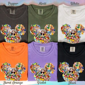 May include: Six t-shirts in various colors: pepper, moss, white, burnt orange, violet, and black. Each shirt features a Mickey Mouse head design filled with cartoon characters. The shirts are labeled with their respective color names.