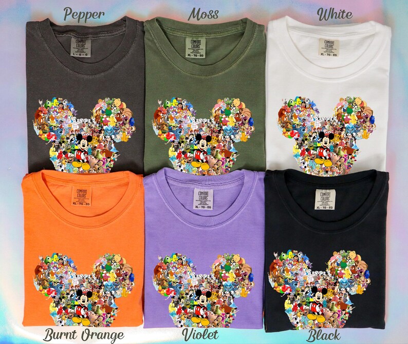 May include: Six t-shirts in various colors: pepper, moss, white, burnt orange, violet, and black. Each shirt features a Mickey Mouse head design filled with cartoon characters. The shirts are labeled with their respective color names.