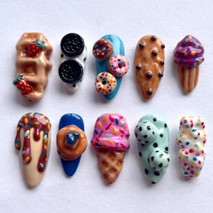 May include: Ten colourful nail charms featuring various food designs, including a waffle, a cookie, a doughnut, an ice cream cone, and a sprinkle-covered treat.