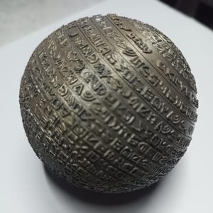 Peut inclure: Une sphère en bronze foncé avec du texte stylisé gravé sur sa surface. La surface de la sphère est divisée en bandes, chacune remplie de gravures complexes. L'effet général est celui d'un artefact ancien ou d'un objet décoratif.