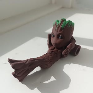 Baby Groot 3D printed figurine resting on a log, made with Rosewood wood PLA, perfect for collectors and fans of Guardians of the Galaxy