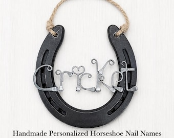 May include: A black metal horseshoe with a jute rope hanger. The center features the word Cricket formed from bent horseshoe nails. The letters are crafted from individual nails, with the letter i topped by a small heart-shaped nail detail.