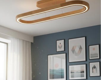 May include: A modern, wooden ceiling light fixture with an oval shape and integrated LED lighting. The light is suspended from the ceiling and has a warm, natural wood finish. The fixture is designed to provide ambient lighting in a contemporary living space.