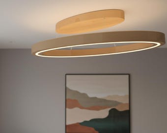 May include: Modern, oval-shaped wooden ceiling light fixture with a smaller, matching wooden disc above it. The larger oval has a bright, white light strip around its inner edge. The fixture is suspended from the ceiling.