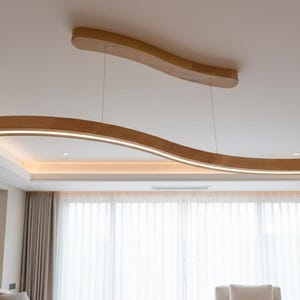 May include: A contemporary light fitting, crafted from wood, with a flowing, wave-like design, suspended from a white ceiling. The fixture has a warm, natural wood tone and emits a soft, diffused light. Suitable for modern interiors.