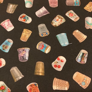 May include: A black fabric with a repeating pattern of colorful thimbles. The thimbles are decorated with various designs, including flowers, cherries, and geometric patterns.