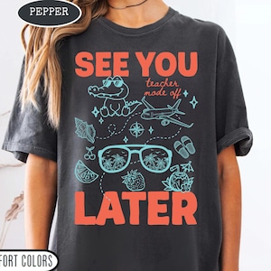 Op de afbeelding: Donkergrijs t-shirt met de woorden "SEE YOU LATER" in koraal. Het shirt heeft een cartoon alligator, zonnebril, een vliegtuig en andere zomerse graphics in turquoise.
