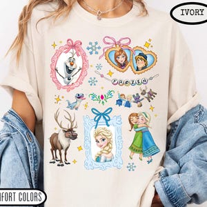 Puede incluir: Camiseta de color marfil con gr&aacute;ficos coloridos de personajes y elementos de la pel&iacute;cula animada "Frozen". El dise&ntilde;o incluye im&aacute;genes de Olaf, Anna, Elsa, Kristoff y Sven, junto con la palabra "FROZEN".