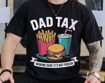 May include: Black t-shirt with a graphic featuring the text "DAD TAX" above a burger, fries, and a drink. The phrase "MAKING SURE IT'S NOT POISON" is below the graphic. The shirt is a casual style.