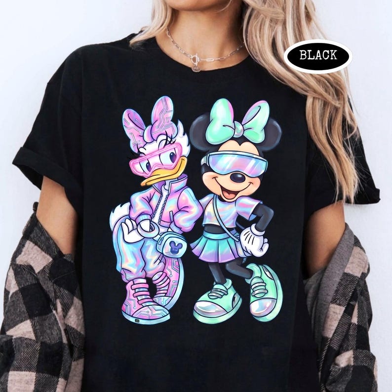 May include: Black t-shirt featuring a colorful graphic of Daisy Duck and Minnie Mouse in futuristic outfits. The characters wear sunglasses and matching pastel-colored clothing. The word "BLACK" is printed on the shirt.